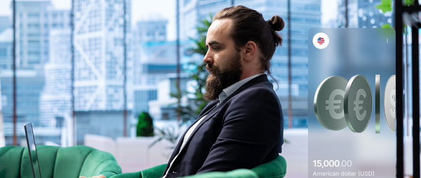 Man with a beard and bun in a suit sits on a green chair, using a laptop in a smart money concepts trading environment. A digital screen displays currency symbols and $15,000 USD. Bright, modern office.