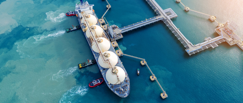 Aerial top-down view of a large LNG tanker ship docked at a marine terminal pipeline system, representing global supply logistics in the future natural gas market.