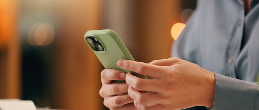 Close-up of a trader's hands holding a light green smartphone while managing their portfolio to harness The Compounding Effect in financial markets.