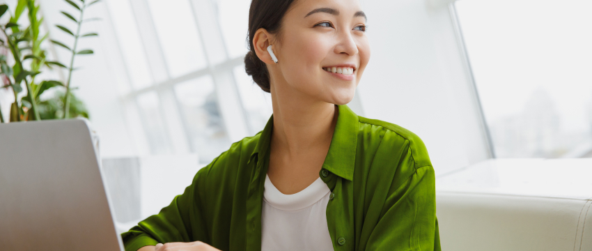 Smiling trader wearing an earbud next to a laptop in a bright office